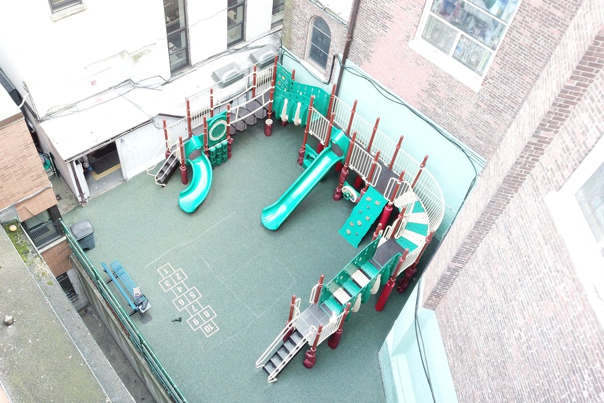 Oblique aerial of the old courtyard — teal slides, red posts, hopscotch grid visible.
