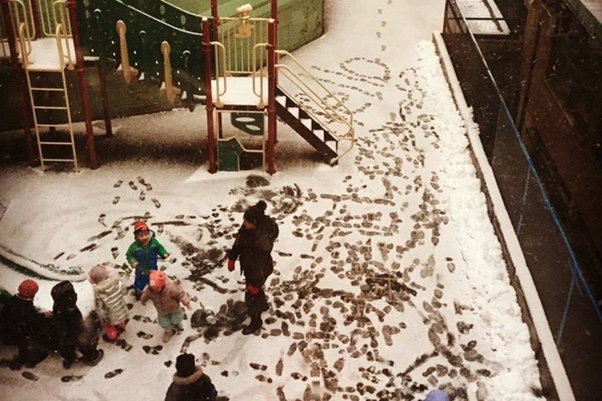 Aerial of children and a teacher playing in snow on the old courtyard surface.