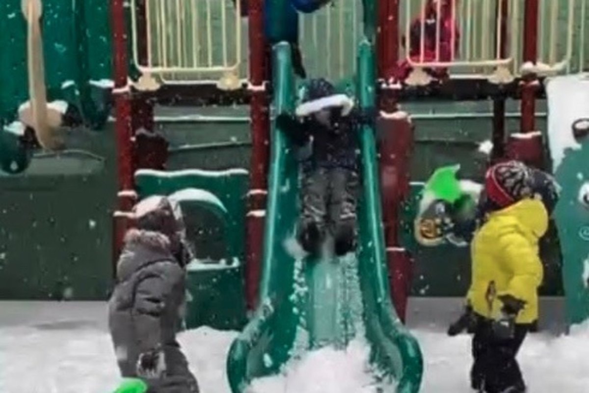 Children climbing up a snowy green slide on the old structure.