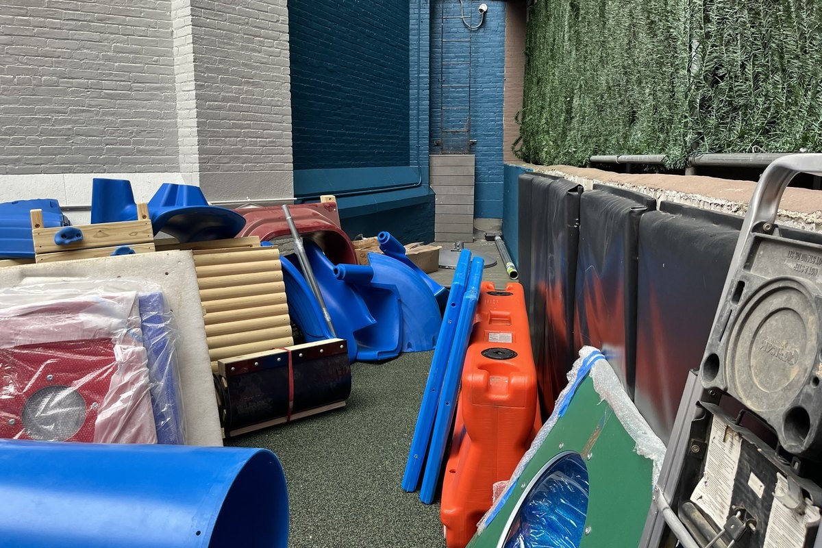 New PlayWood Plus components — blue slides, lumber, panels — staged in the courtyard before installation.