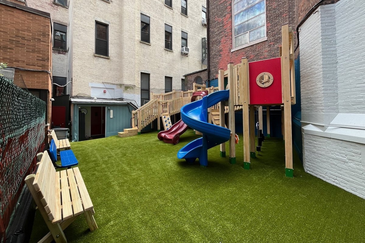 Ground-level view of the finished structure — blue spiral slide, red slide, wood benches, brick building surround.