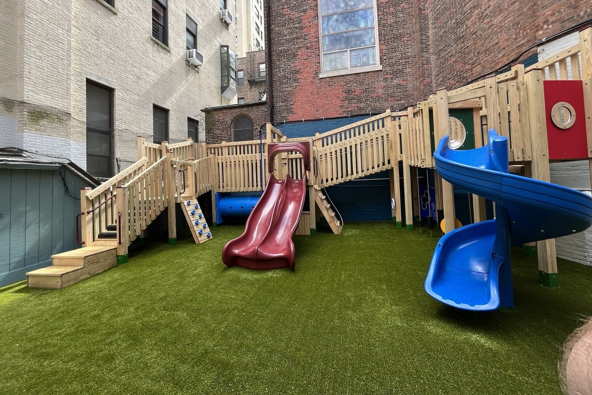 Wider angle showing full structure with red and blue slides, ramp stairs, benches, brick backdrop.