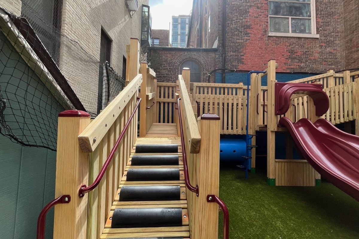 Close-up of the rubber-treaded entry staircase with burgundy handrails, red slide visible behind.