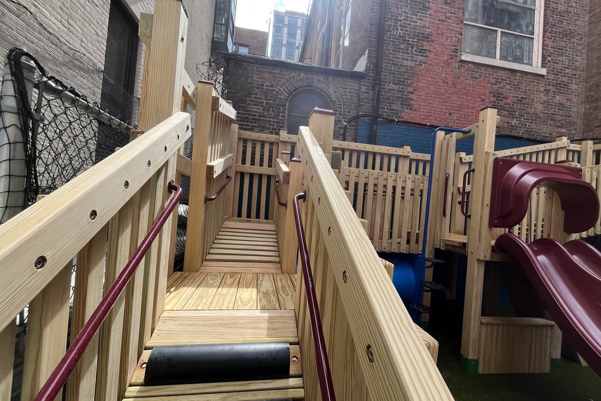 Looking up the ramp and stair run from ground level — wood deck, rubber treads, burgundy rails, red slide at right.