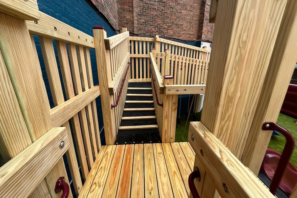 View from the upper deck looking down the stair run — beautiful wood grain, rubber treads, burgundy handrails.