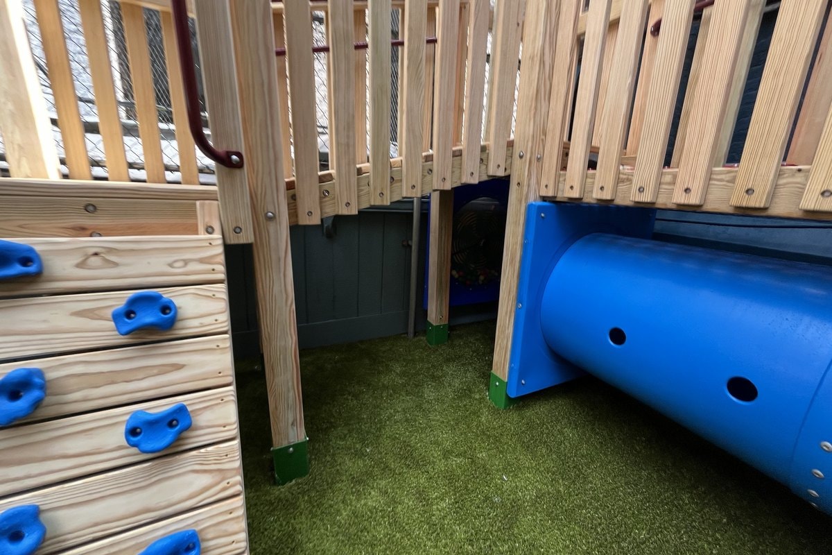 Ground-level detail — blue climbing wall with holds at left, blue horizontal tunnel at right, under-deck space visible center.