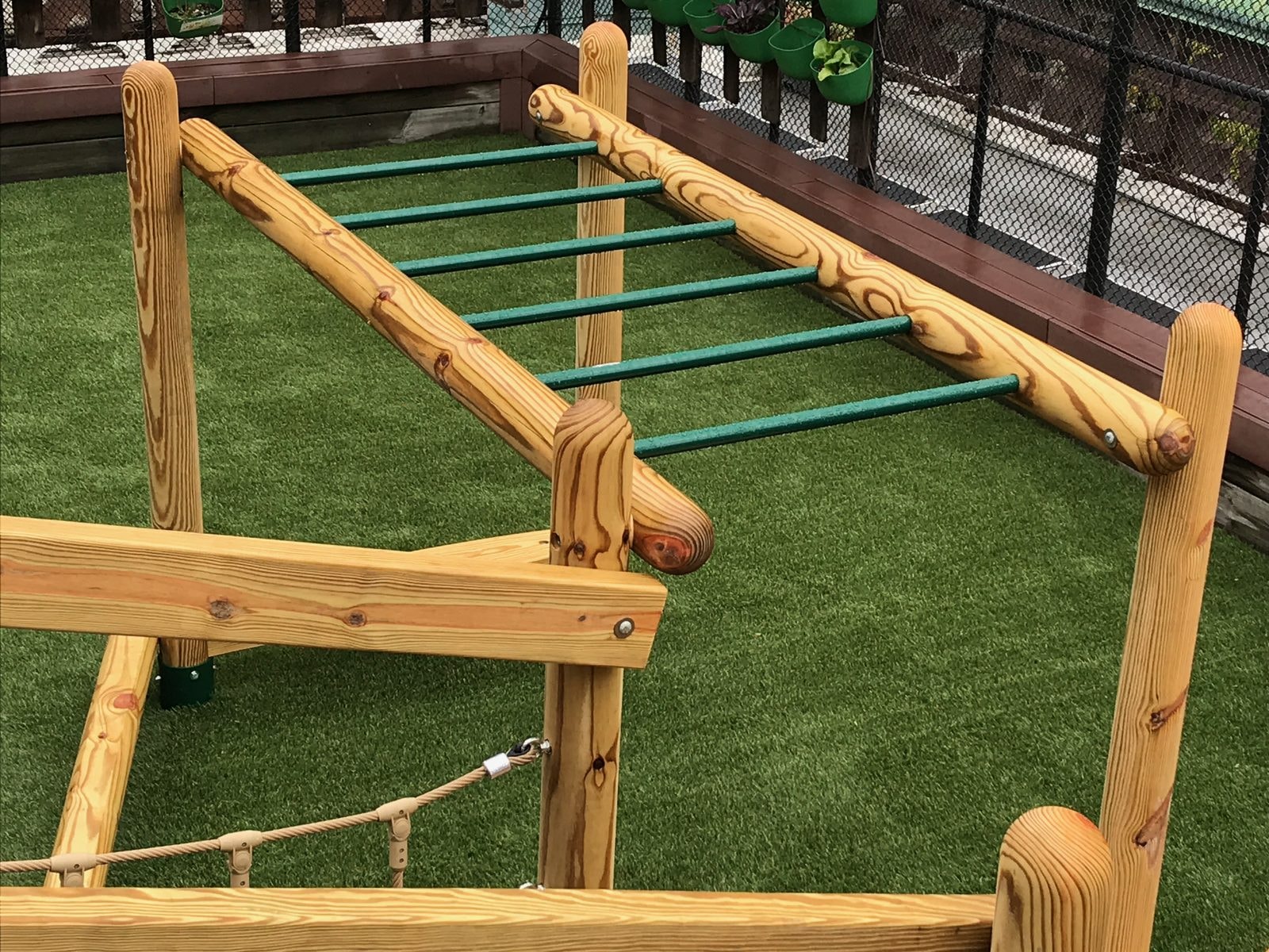 Hand-over-hand ladder built on round wooden posts with green rungs.