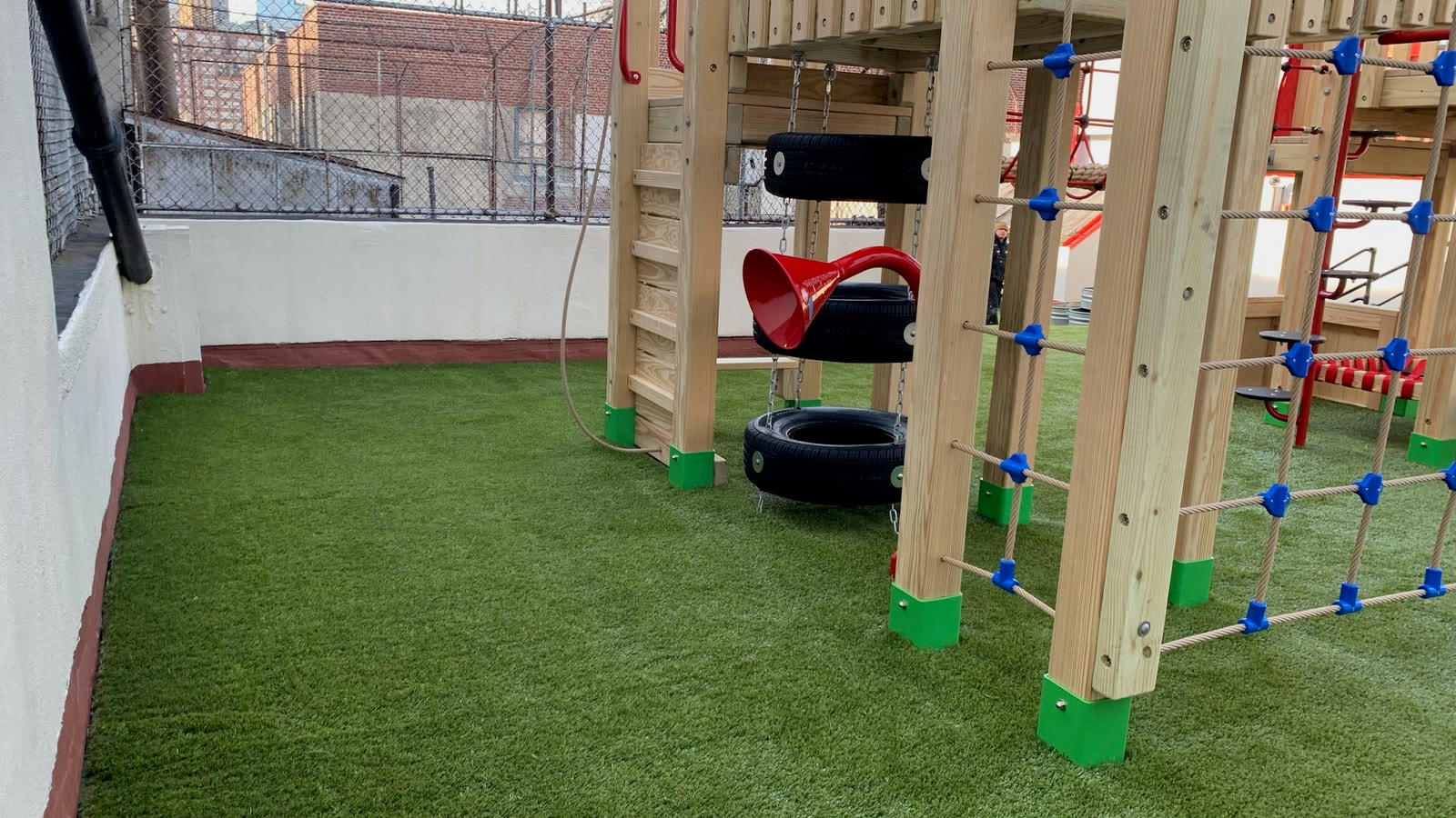 Children climbing the rope net and tire swing on the Little Red School House rooftop playground.