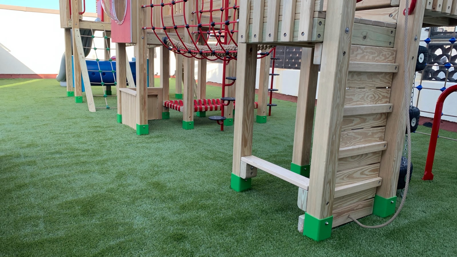 Detail view of the custom wood play structure at Little Red School House, showing rope obstacles and climbing elements.