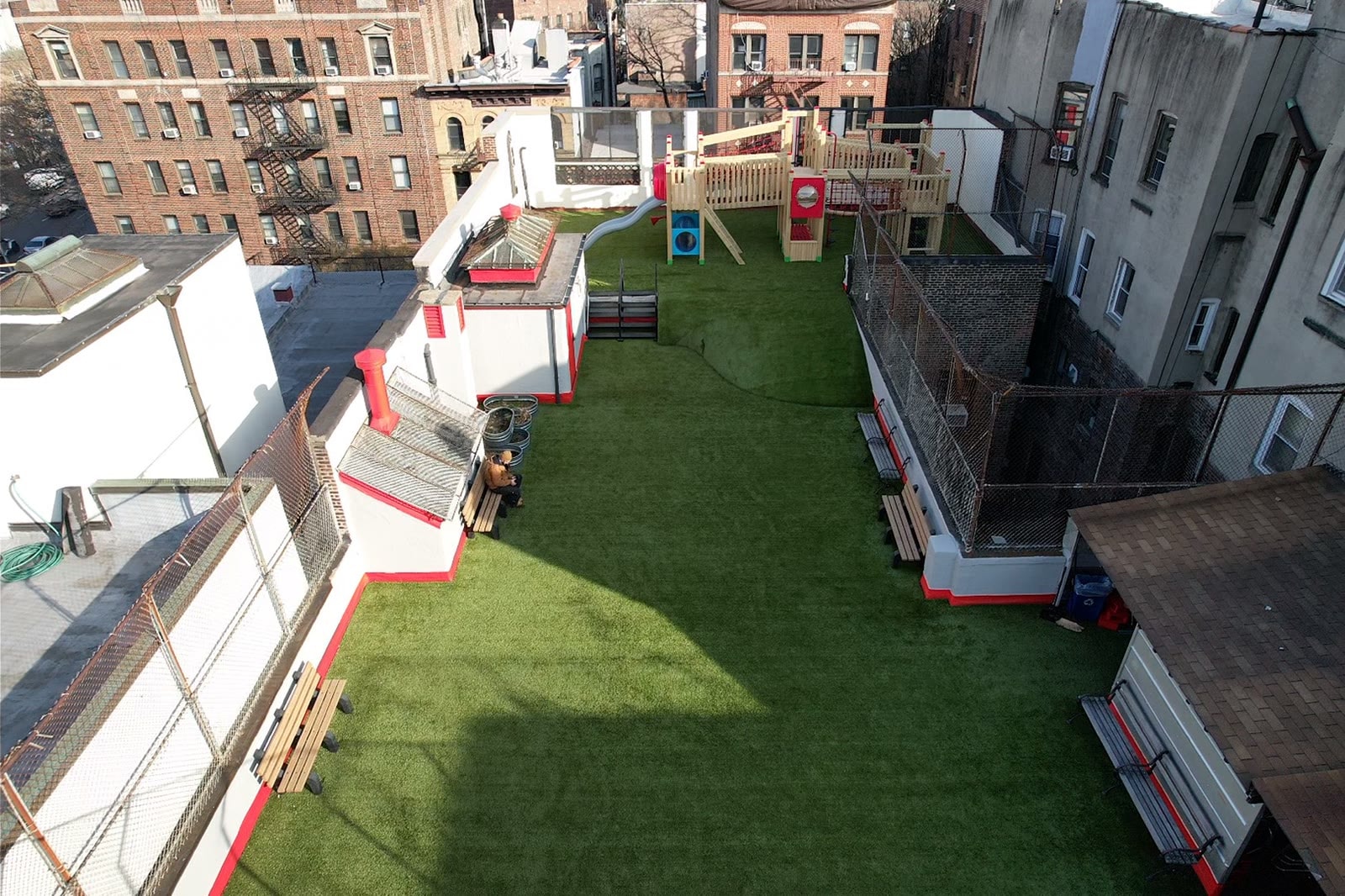 Wide view of the Little Red School House rooftop playground with artificial turf and the urban context.