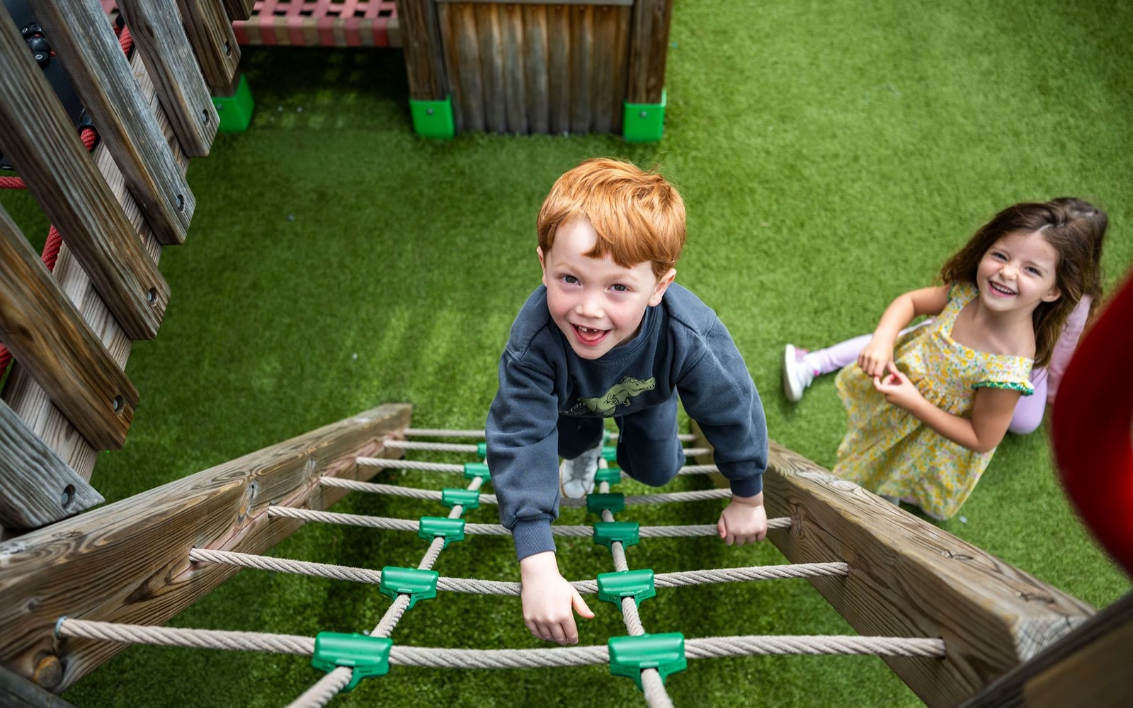 Children crossing the rope bridge on the Little Red School House rooftop play structure.