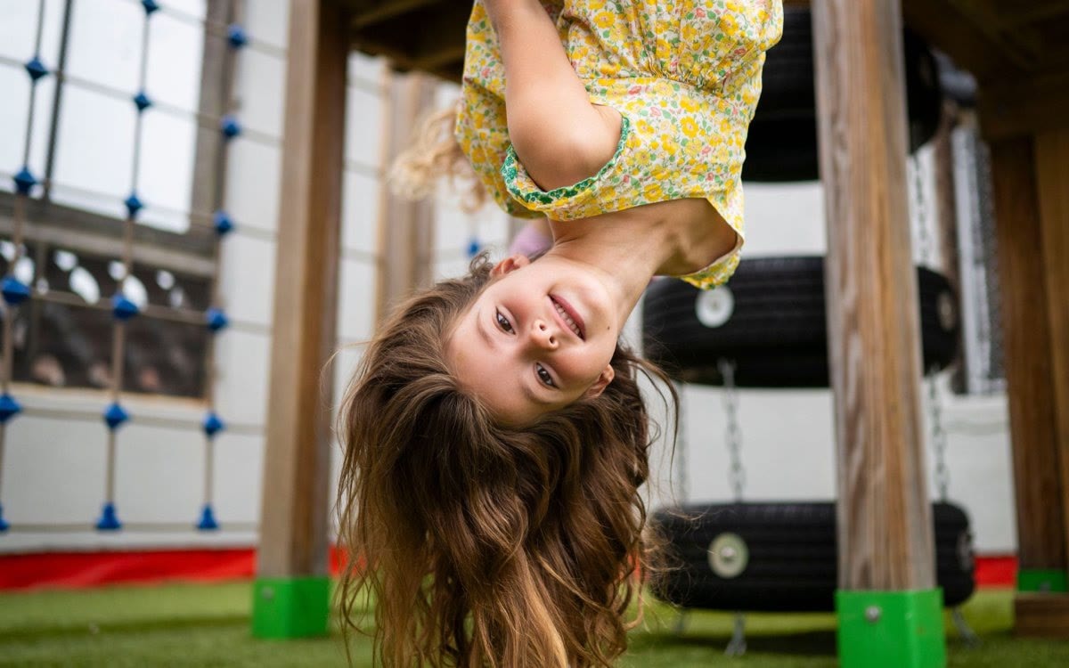A child hanging upside down from the climbing elements on the Little Red School House playground.