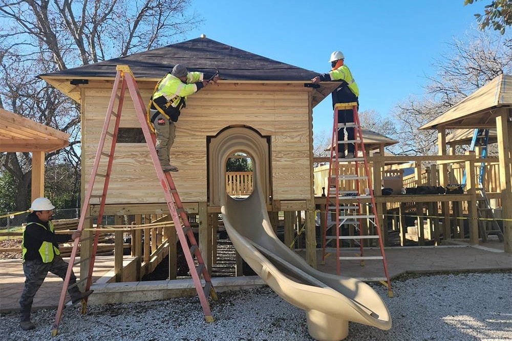 Crew roofing a house beside a tube slide