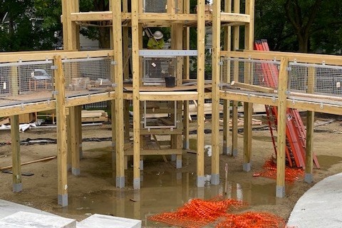 A timber play tower frame under construction on an active site.